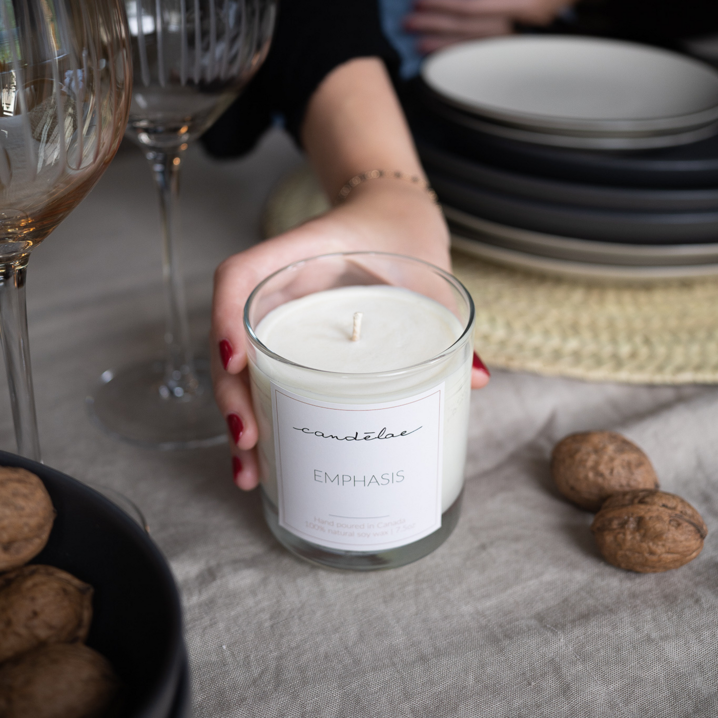 A woman is holding candēlae Emphasis candle on a table that is set with beautiful plates