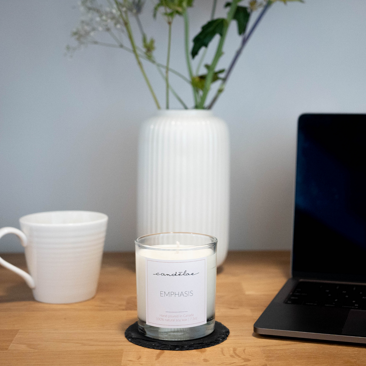 The premium soy wax candle from candēlae is display on a desk next to a laptop and a cup of tea
