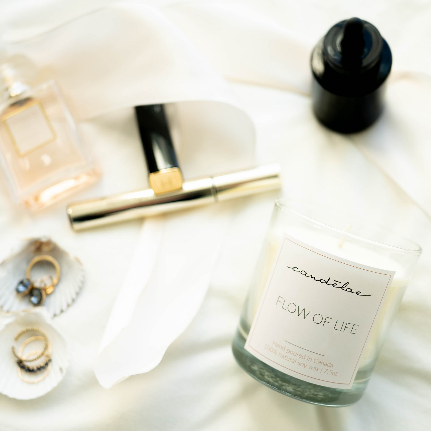 Flow of Life scented candle with essential oils is set on the bed around beautiful rings, earrings