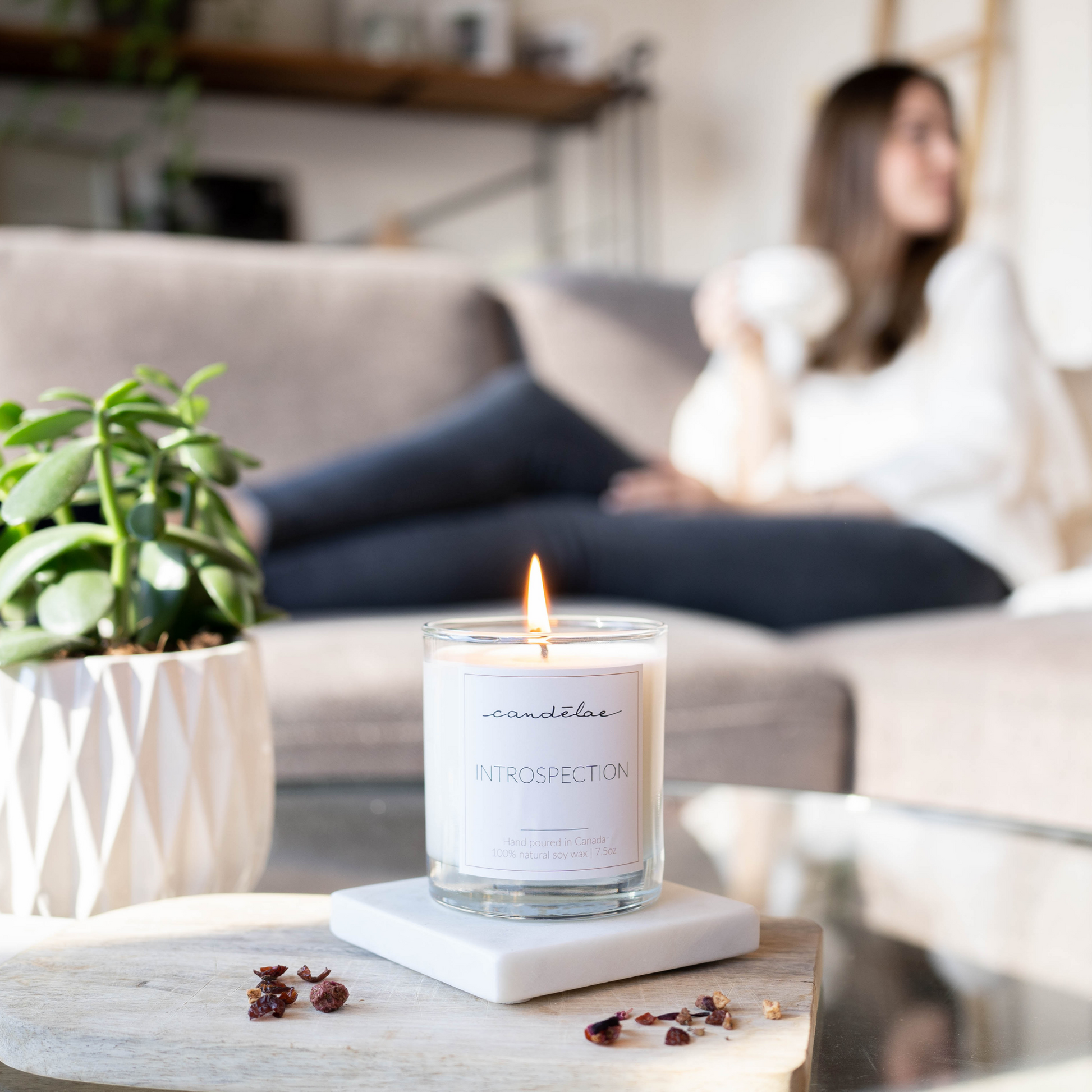 A woman is drinking her tea while she is relaxing with her Introspection candle from candēlae