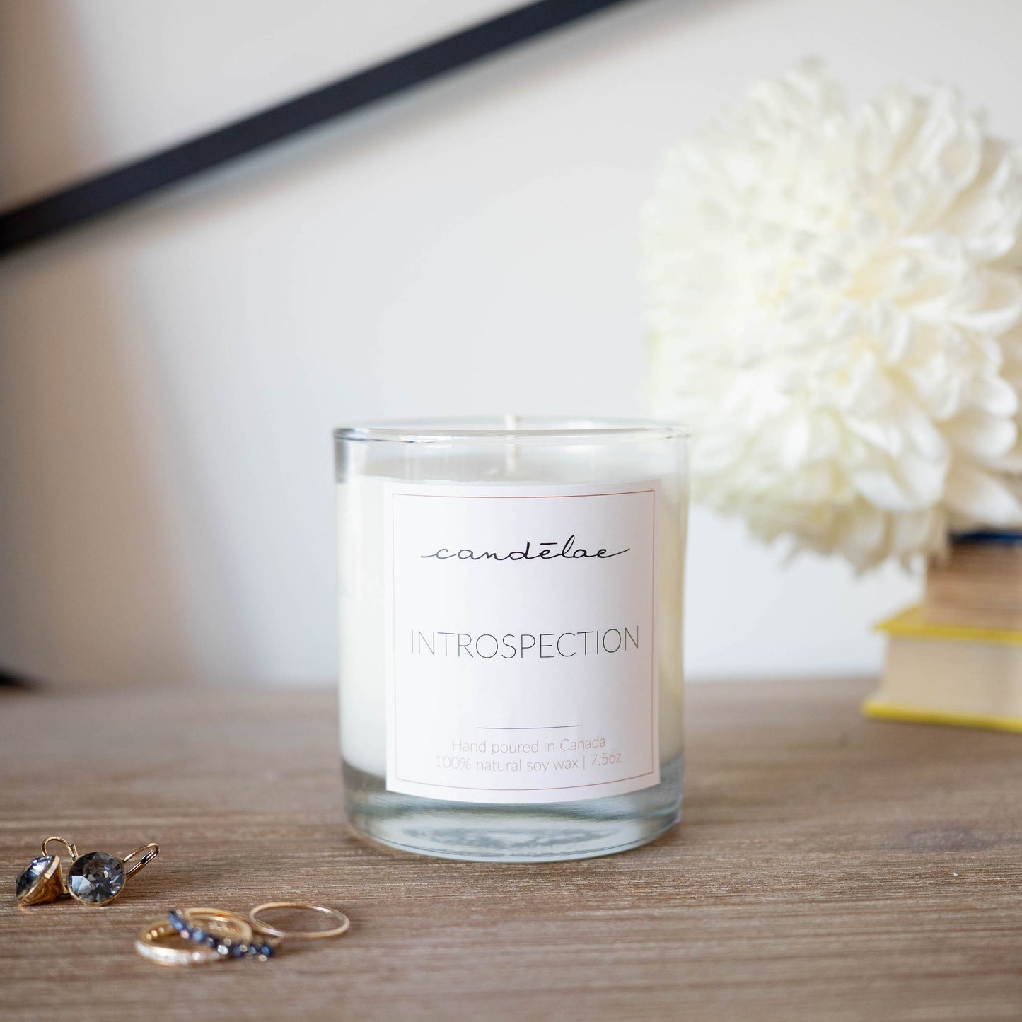 The soy wax scented candle from candēlae named Introspection is set around rings and earrings