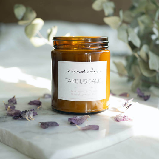 The soy wax candle by candēlae with notes of Bergamot and Frankincense is set around rose petals